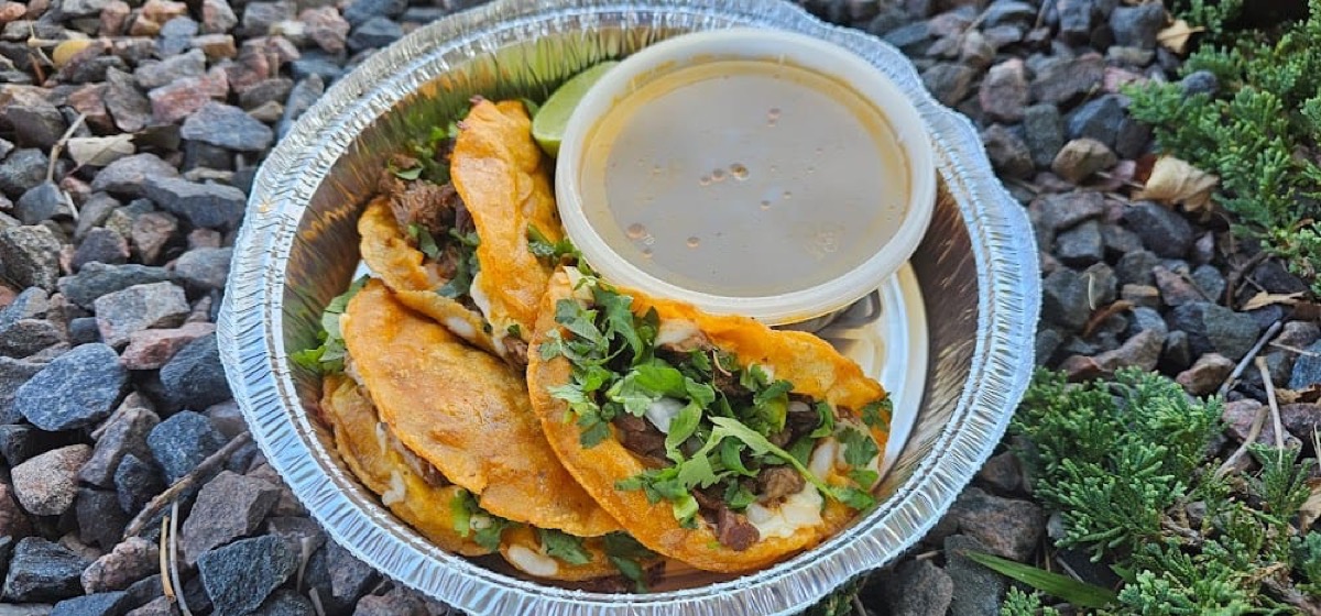 Quesabirria tacos topped with cilantro, with a lime and a cup of consommé