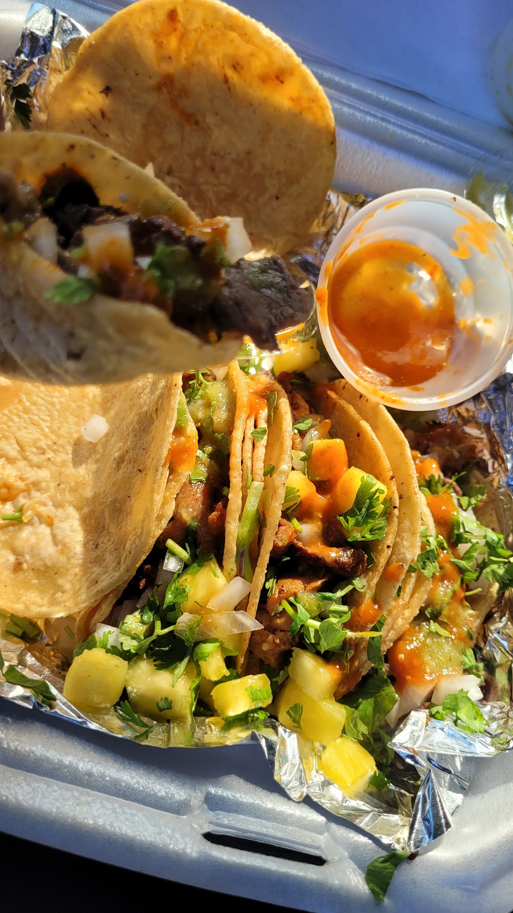 Al pastor tacos with pineapple and a cup of salsa in a to-go box