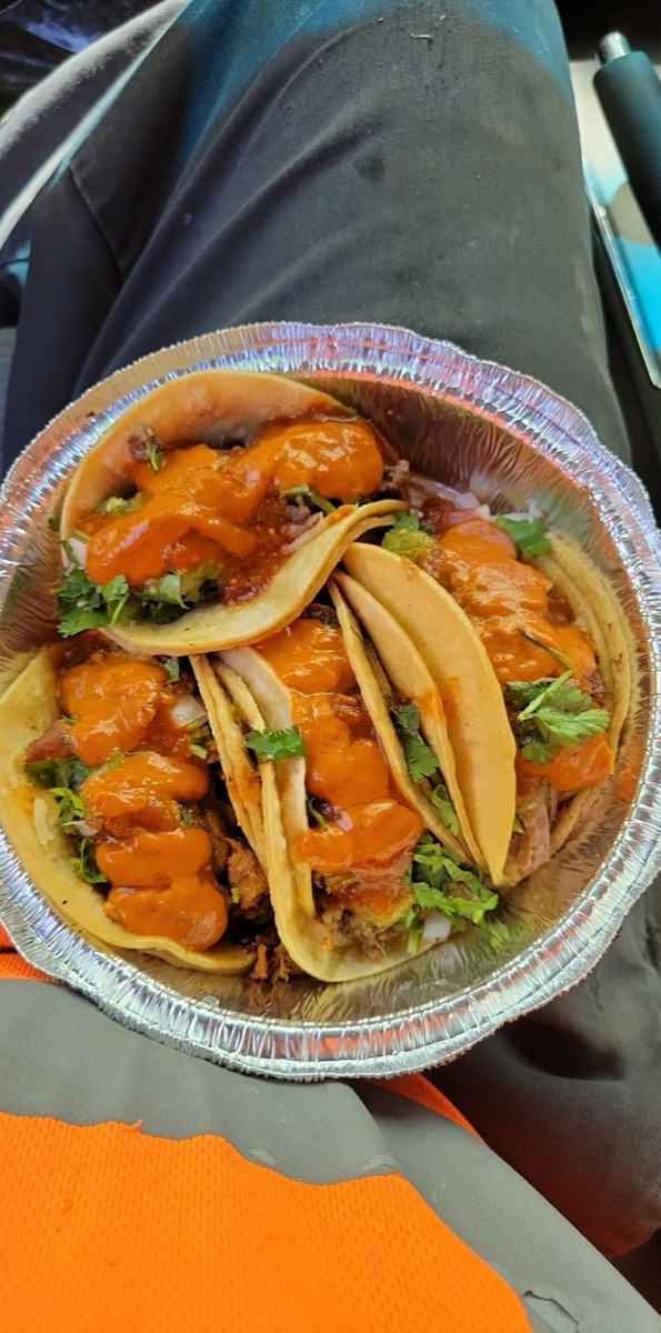 A foil tray of tacos covered in red salsa and cilantro