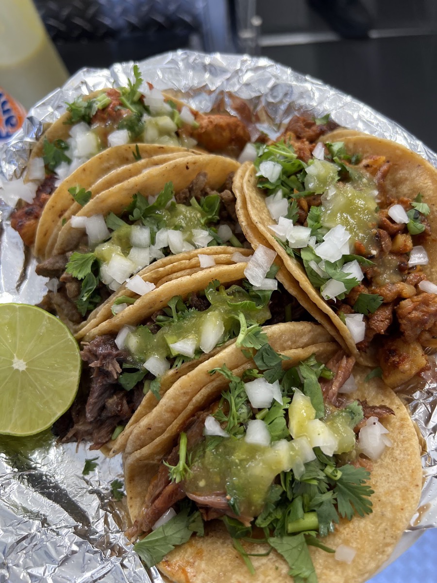 Five street tacos topped with cilantro, onion and salsa, with a lime, on foil